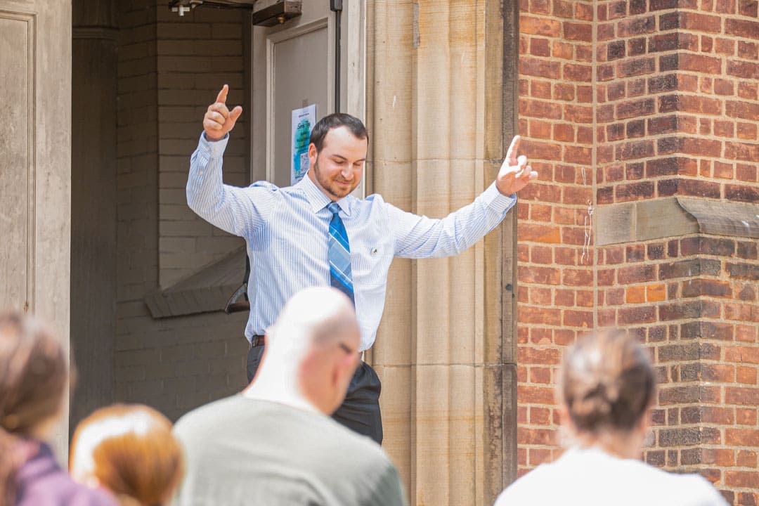 male in a blue tie with his hands up in the air