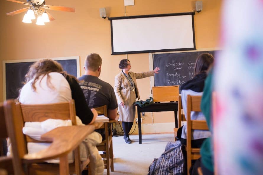 Senior teacher helping young african man at the library with friends. Group of university guys and girl sitting at desk while mature professor helping them in reading hall. Group of multiethnic high school students studying with lecturer.
