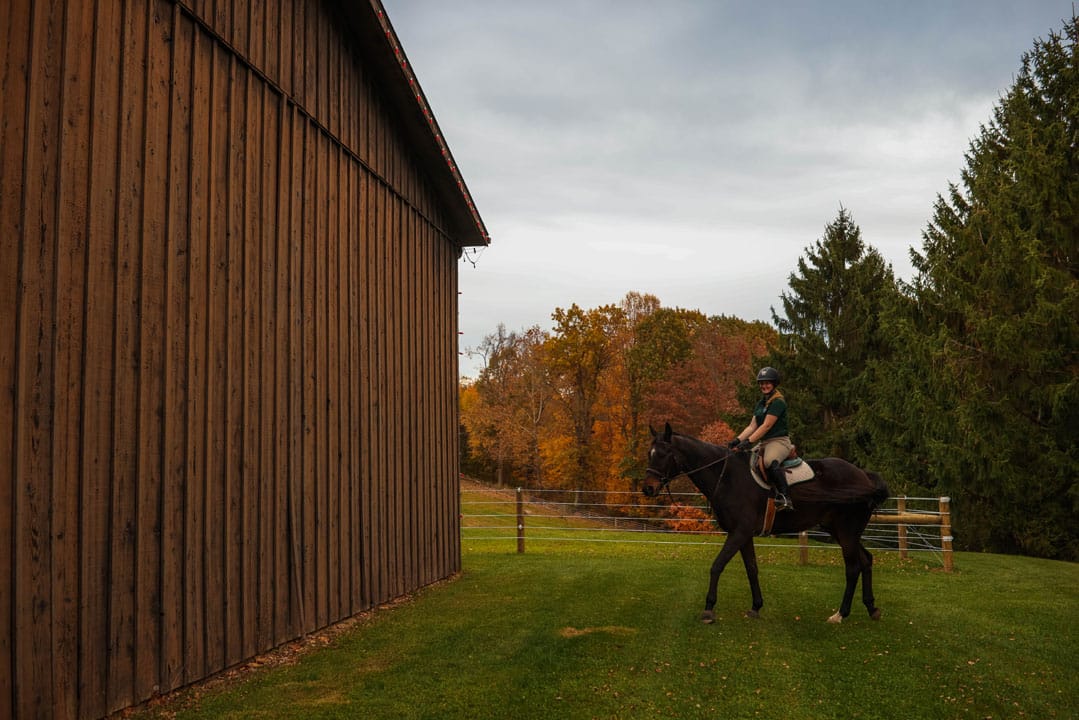 female riding a horse by a barn